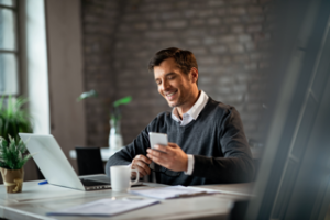 happy-businessman-texting-mobile-phone-while-working-laptop-office Small